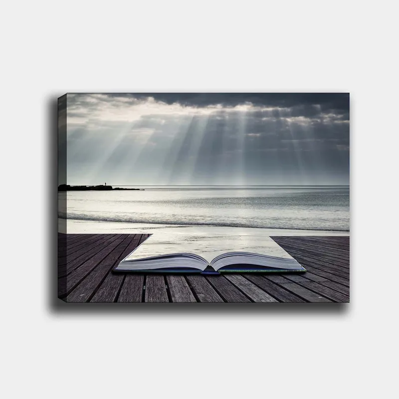 Lærred 70x100 cm - Åben bog liggende på en træmole ved havet, omgivet af bløde lysstråler fra en overskyet himmel, Grå / Blå / Hvid