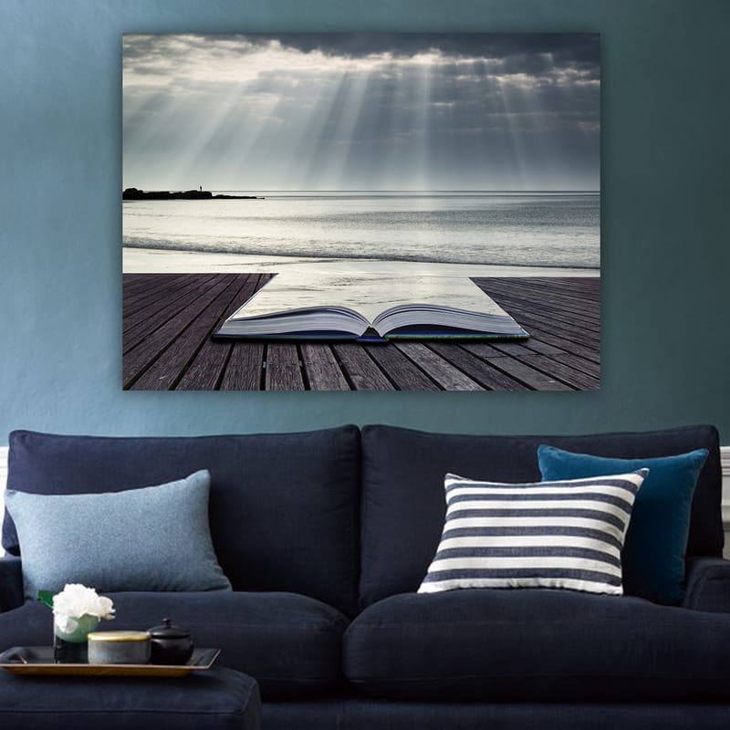 Lærred 70x100 cm - Åben bog liggende på en træmole ved havet, omgivet af bløde lysstråler fra en overskyet himmel - Grå / Blå / Hvid - Boligtilbehør - Billeder & kunst - Billeder på lærred