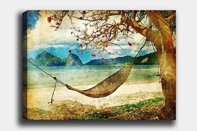 Lærred 70x100 cm - Afslappende hængekøje hængende mellem trægrene på en smuk strand med fjerne bjerge i baggrunden, Grøn / Brun / Blå