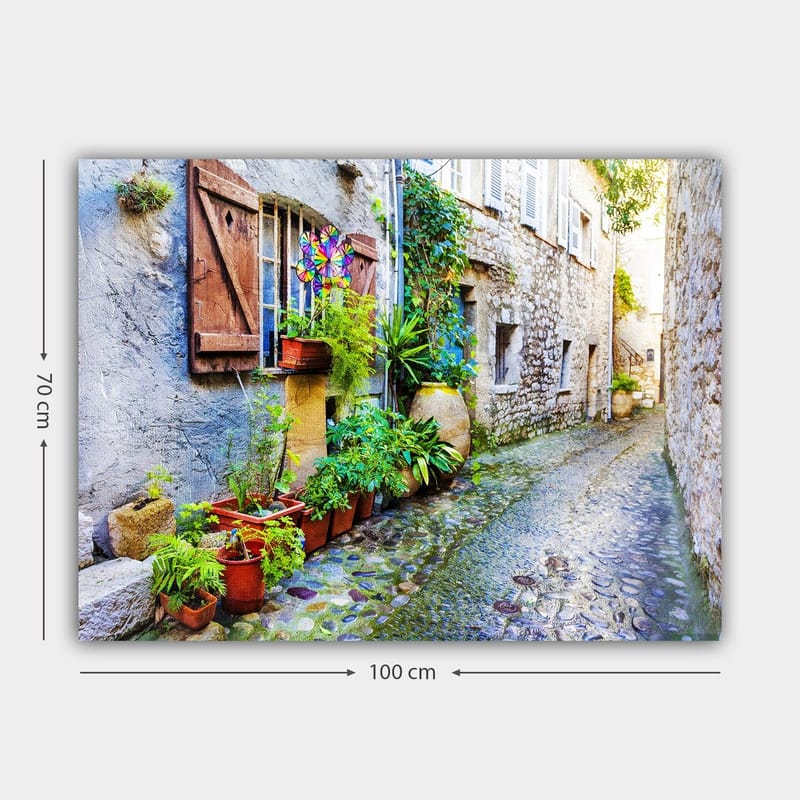 Lærred 70x100 cm - Charmerende gyde med stenhuse og blomsterkrukker skaber en livlig atmosfære - Grøn / Blå / Beige - Boligtilbehør - Billeder & kunst - Billeder på lærred