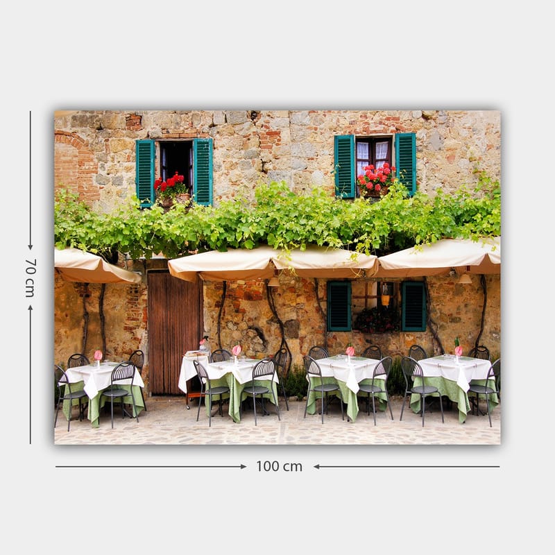 Lærred 70x100 cm - Charmerende udendørs spiseplads med hvide borde og grønne duge foran en gammel stenbygning med mørkegrønne skodder - Mørkegrøn / Hvid / Teglrød - Boligtilbehør - Billeder & kunst - Billeder på lærred