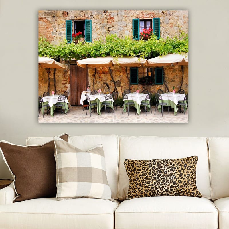 Lærred 70x100 cm - Charmerende udendørs spiseplads med hvide borde og grønne duge foran en gammel stenbygning med mørkegrønne skodder - Mørkegrøn / Hvid / Teglrød - Boligtilbehør - Billeder & kunst - Billeder på lærred