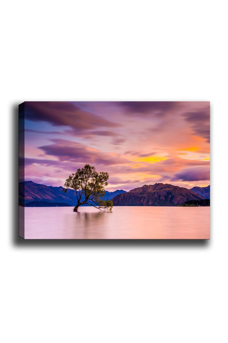 Lærred 70x100 cm - Ensom træstamme i en spejlblank sø med fjerne bjerge i baggrunden under en farverig himmel ved solnedgang, Lilla / Grøn / Orange