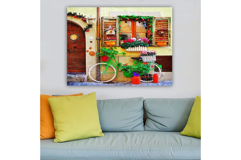 Lærred 70x100 cm - Farverig cykel pyntet med blomster og potter foran en charmerende væg med vinduer og dekorationer - Grøn / Lyserød / Orange - Boligtilbehør - Billeder & kunst - Billeder på lærred