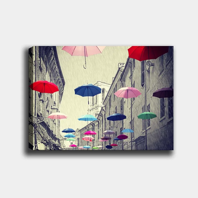 Lærred 70x100 cm - Farverige paraplyer svæver over en grå bygade, Rød / Blå / Lyserød