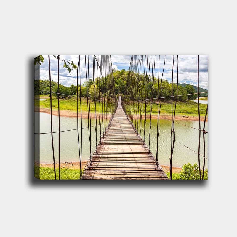 Lærred 70x100 cm - Hængebro over en rolig sø, omgivet af frodigt grønt, Grøn / Brun / Blå