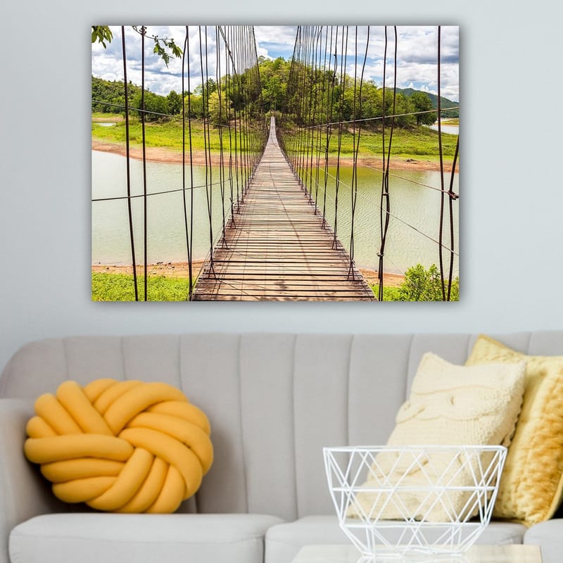 Lærred 70x100 cm - Hængebro over en rolig sø, omgivet af frodigt grønt - Grøn / Brun / Blå - Boligtilbehør - Billeder & kunst - Billeder på lærred