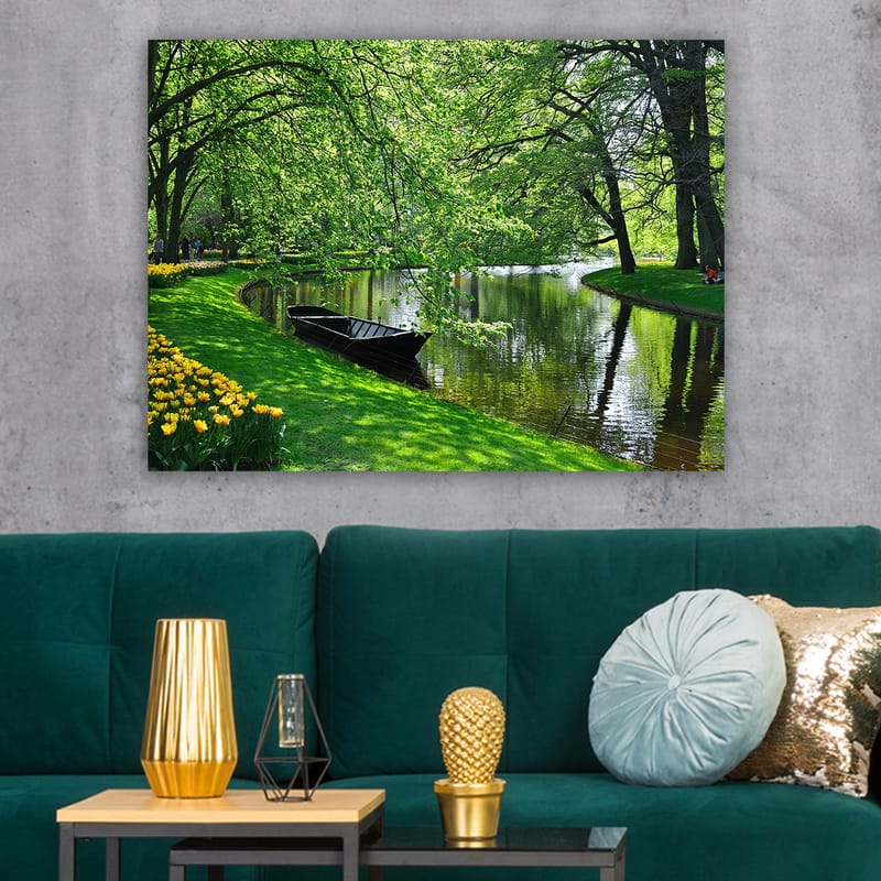 Lærred 70x100 cm - Idyllisk søscene med en båd, der ligger stille på en grøn bred omgivet af træer og blomster - Grøn / Sort / Gul - Boligtilbehør - Billeder & kunst - Billeder på lærred