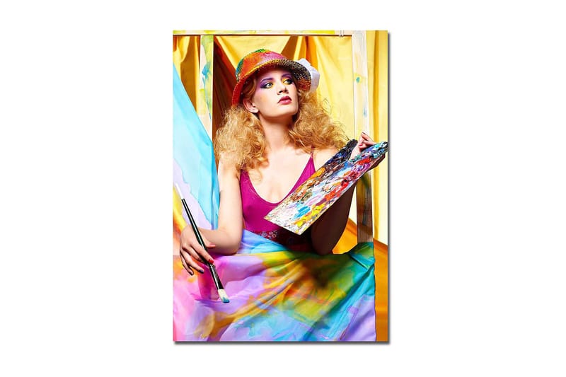 Lærred 70x100 cm - Kreativ kvinde der maler med en palet i hånden, omgivet af farverige stoffer, Lyserød / Blå / Gul