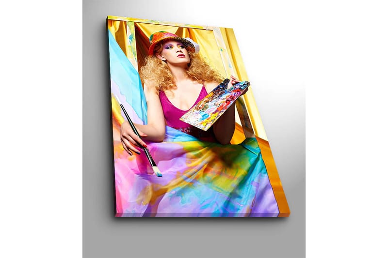 Lærred 70x100 cm - Kreativ kvinde der maler med en palet i hånden, omgivet af farverige stoffer - Lyserød / Blå / Gul - Boligtilbehør - Billeder & kunst - Billeder på lærred
