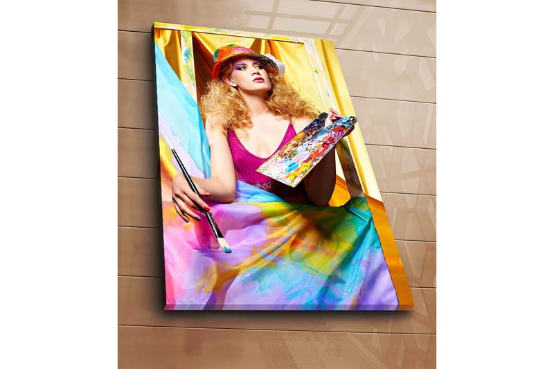 Lærred 70x100 cm - Kreativ kvinde der maler med en palet i hånden, omgivet af farverige stoffer - Lyserød / Blå / Gul - Boligtilbehør - Billeder & kunst - Billeder på lærred