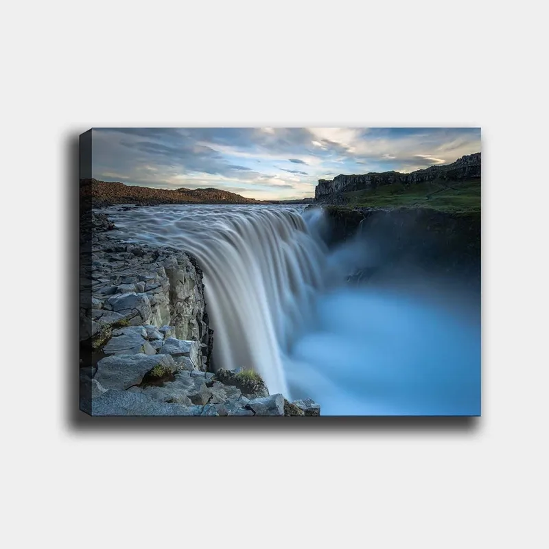 Lærred 70x100 cm - Majestætisk vandfald, der flyder over klipper i naturskønne omgivelser, Blå / Grå / Hvid