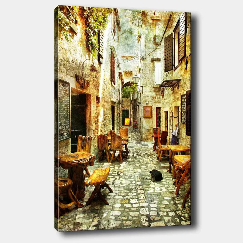 Lærred 70x100 cm - Malerisk gyde med træborde og -stole, omgivet af gamle stenhuse, Brun / Grå / Grøn