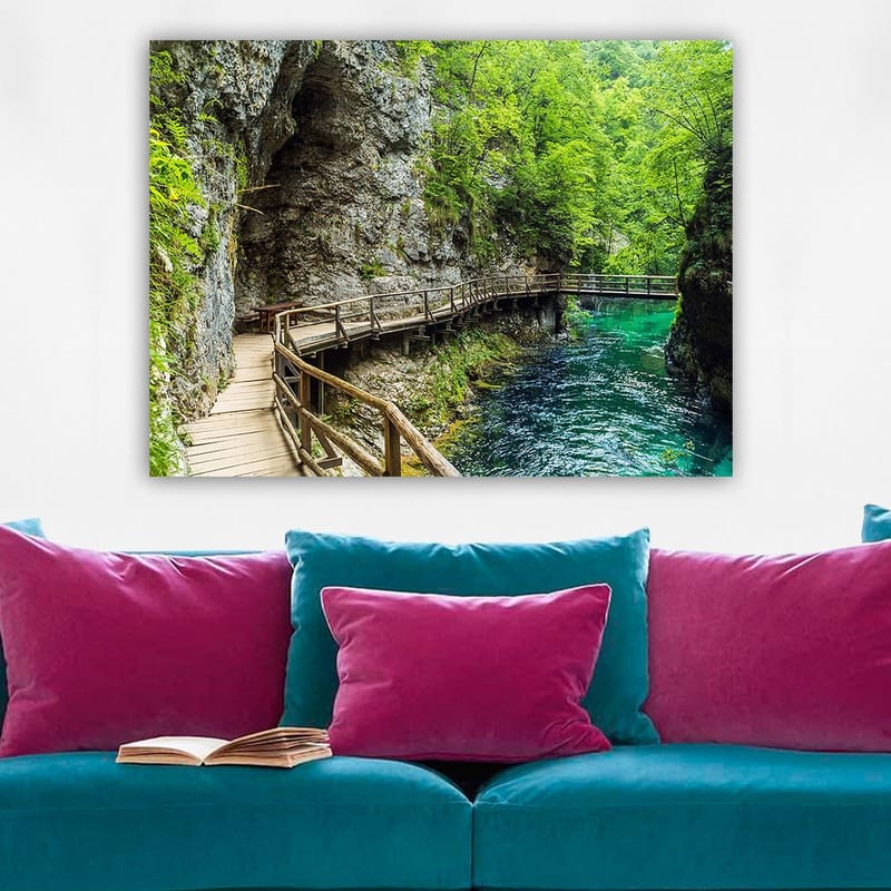Lærred 70x100 cm - Naturskøn udsigt over en træbro, der snor sig gennem en frodig kløft ved en klar, turkis flod - Grøn / Turkis / Grå - Boligtilbehør - Billeder & kunst - Billeder på lærred