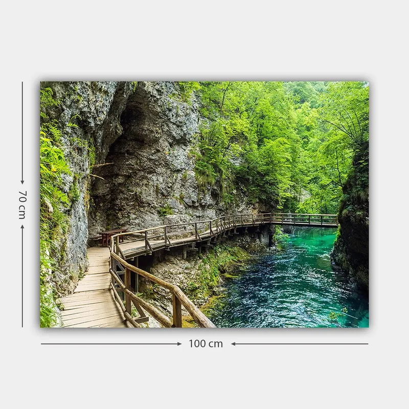 Lærred 70x100 cm - Naturskøn udsigt over en træbro, der snor sig gennem en frodig kløft ved en klar, turkis flod - Grøn / Turkis / Grå - Boligtilbehør - Billeder & kunst - Billeder på lærred