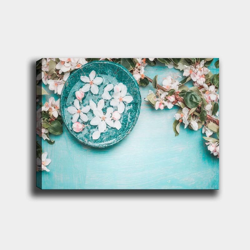 Lærred 70x100 cm - Skål med blomster omgivet af frodige grønne kviste og blomster på en lyseblå baggrund, Turkis / Hvid / Lyserød