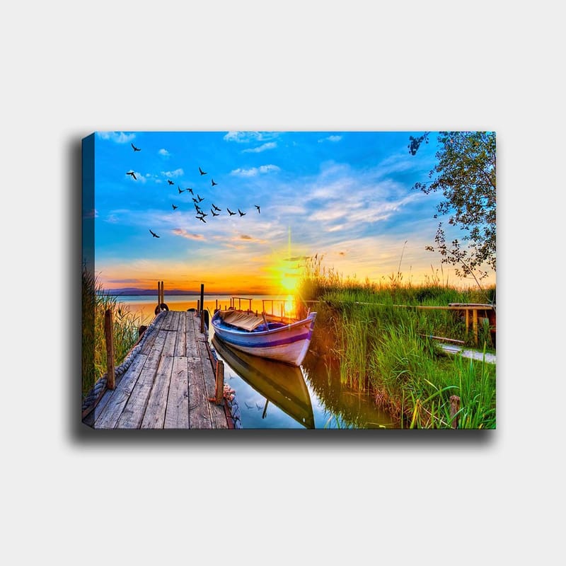 Lærred 70x100 cm - Smuk solnedgang over en rolig sø med en båd ved en træmole omgivet af grønne områder, Blå / Orange / Grøn