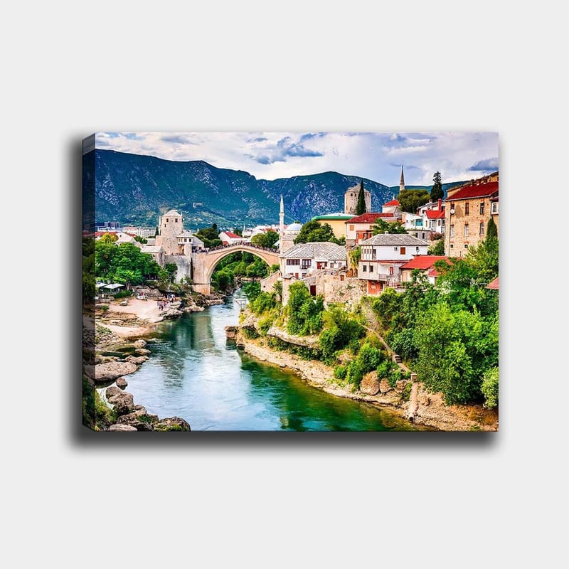 Lærred 70x100 cm - Smuk udsigt over en historisk bro, der spænder over en flod, omgivet af maleriske huse og frodige grønne områder, Grøn / Blå / Rød