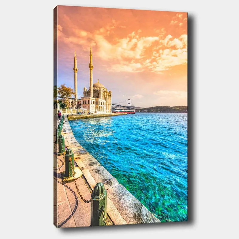 Lærred 70x100 cm - Smuk udsigt over en moské ved vandet med en bro i baggrunden under en farverig himmel, Blå / Orange / Beige