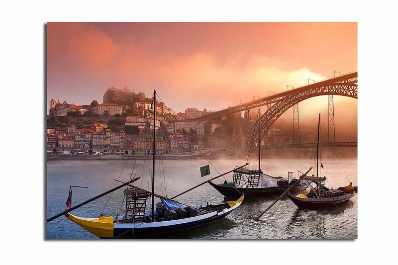 Lærred 70x100 cm - Smuk udsigt over floden med traditionelle både og en majestætisk bro i baggrunden, omgivet af farverige huse, Orange / Blå / Gul
