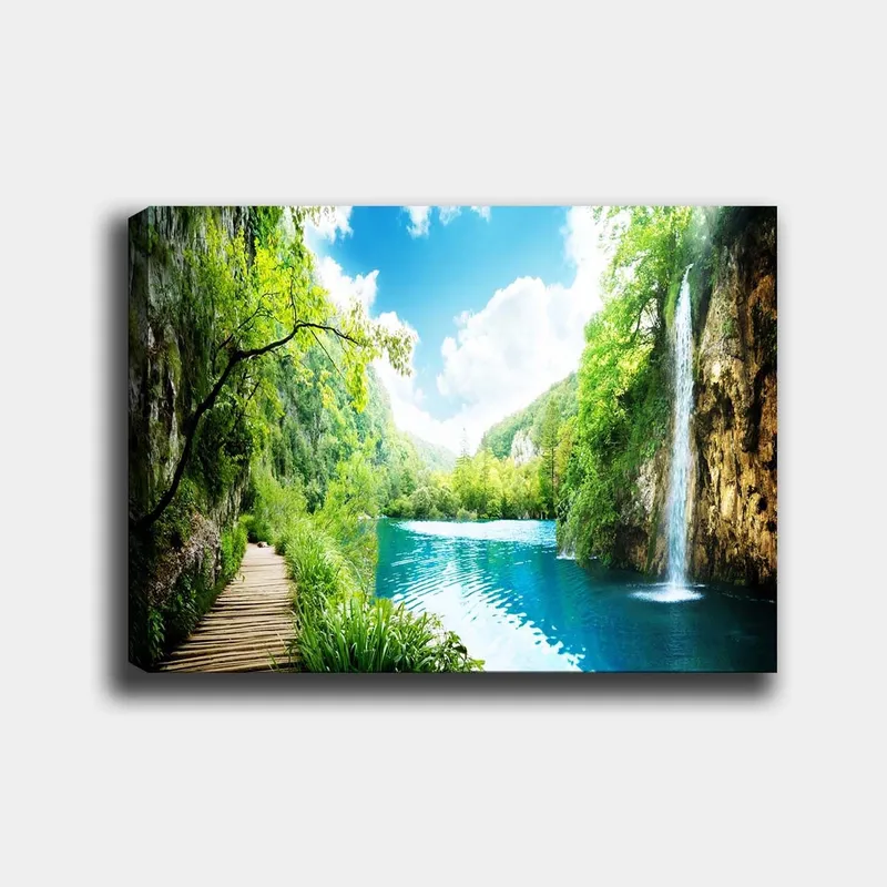 Lærred 70x100 cm - Smukt natursceneri med et vandfald, der løber ud i en klar, blå sø omgivet af frodigt grønt og bjerge, Grøn / Blå