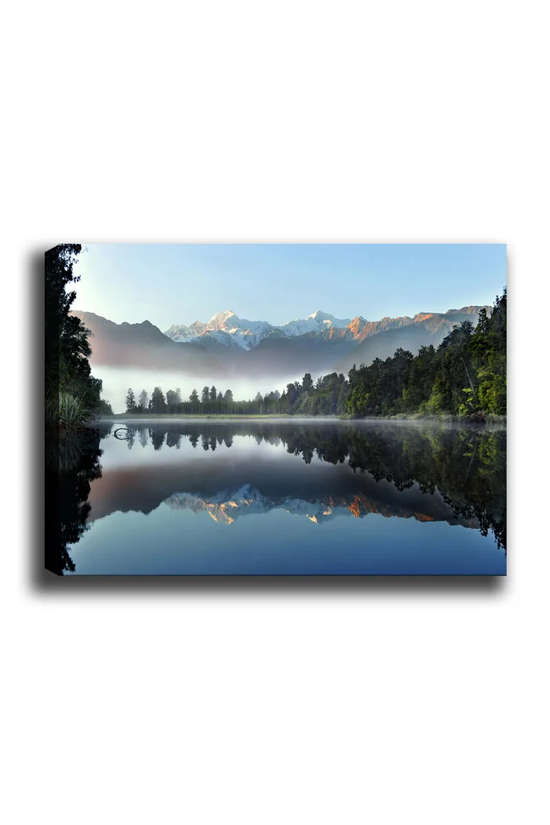 Lærred 70x100 cm - Spejlbillede af majestætiske bjerge spejlet i en rolig sø omgivet af frodig skov, Blå / Grøn / Hvid