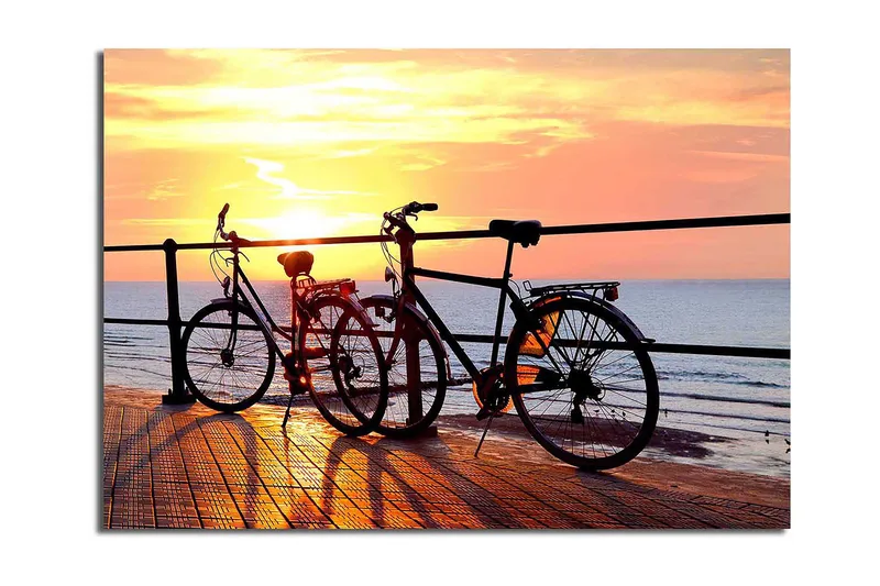 Lærred 70x100 cm - To cykler stående på en mole ved solnedgang over havet, Orange / Sort / Gul