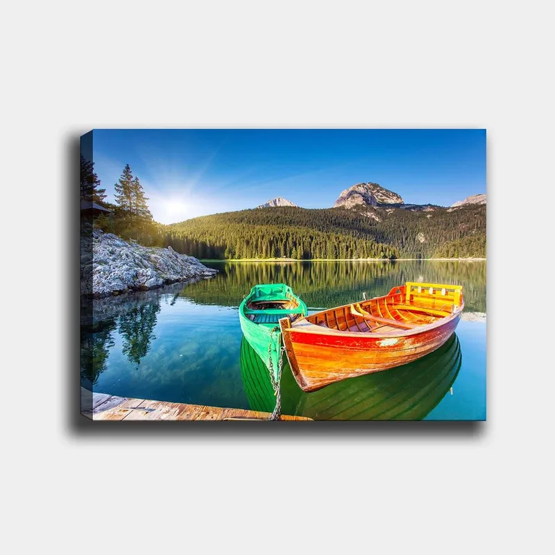 Lærred 70x100 cm - To farverige både ligger stille på en spejlblank sø omgivet af frodige bjerge, Grøn / Orange / Blå