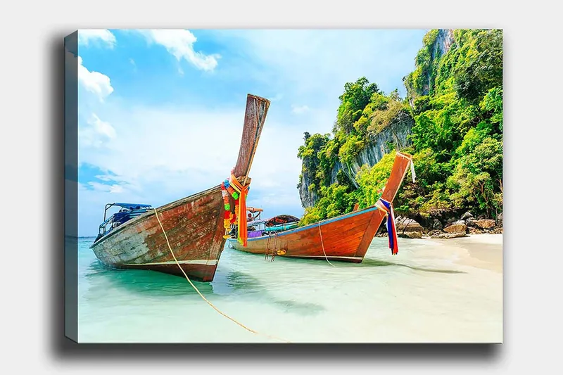 Lærred 70x100 cm - To traditionelle thailandske langbåde på en strand med klipper og frodig vegetation i baggrunden, Brun / Grøn / Blå