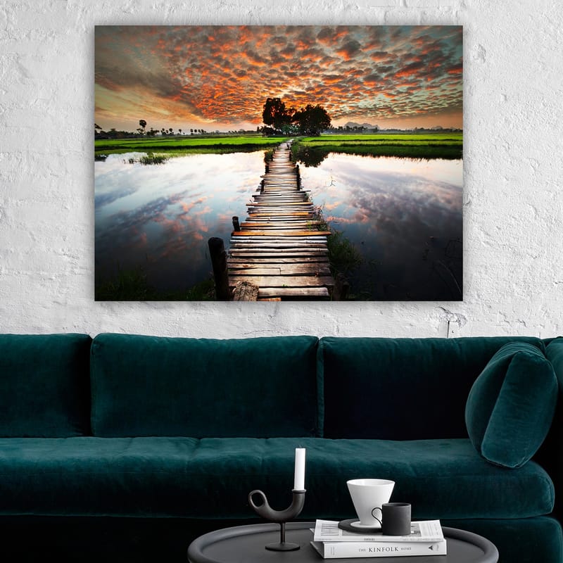 Lærred 70x100 cm - Træbro, der spænder over en spejlblank vandoverflade, omgivet af frodigt grønt og en dramatisk solnedgang - Orange / Grøn / Blå - Boligtilbehør - Billeder & kunst - Billeder på lærred