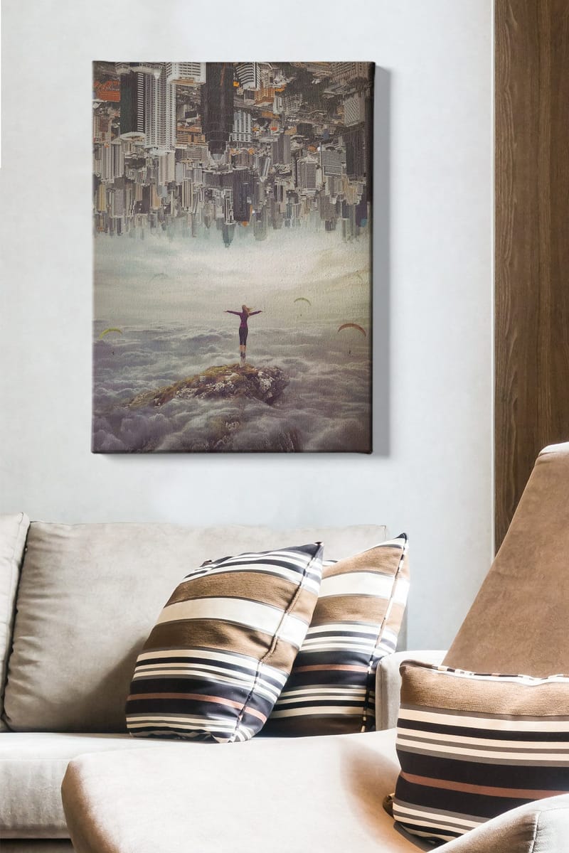 Lærred 70x100 cm - Person stående med udstrakte arme på en klippe over skyerne, med en by i baggrunden, der er vendt på hovedet - Grå / Beige / Mørkeblå - Boligtilbehør - Billeder & kunst - Billeder på lærred