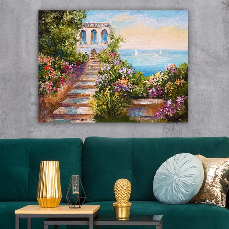 Lærredsbillede 70x100 cm - Smuk trappe omgivet af farverige blomster, der fører ned til havet og en bygning med blå vinduer - Grøn / Lyserød / Blå - Boligtilbehør - Billeder & kunst - Billeder på lærred