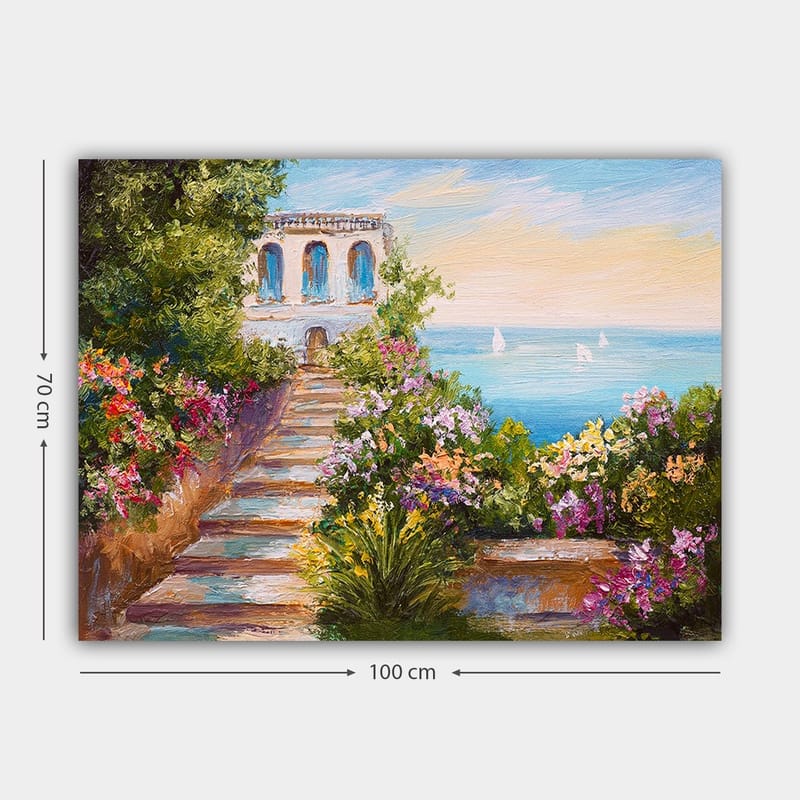 Lærredsbillede 70x100 cm - Smuk trappe omgivet af farverige blomster, der fører ned til havet og en bygning med blå vinduer - Grøn / Lyserød / Blå - Boligtilbehør - Billeder & kunst - Billeder på lærred