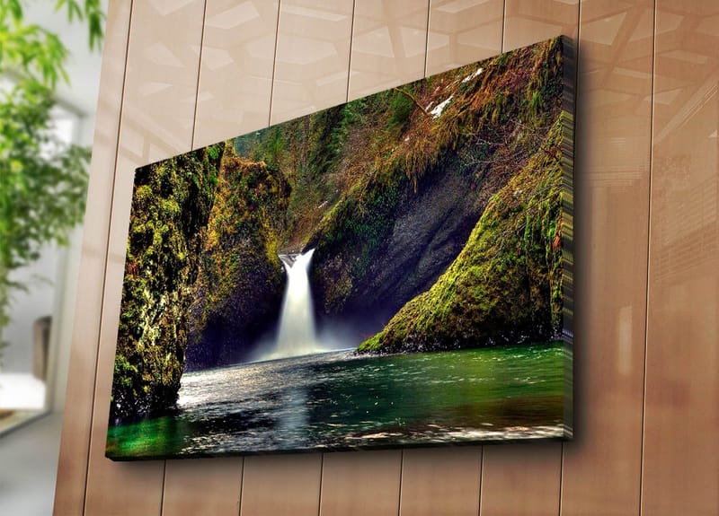 Lærredsbillede 70x100 cm - Smukt vandfald der flyder ned mellem grønne klipper i et naturskønt miljø - Grøn / Blå / Brun - Boligtilbehør - Billeder & kunst - Billeder på lærred