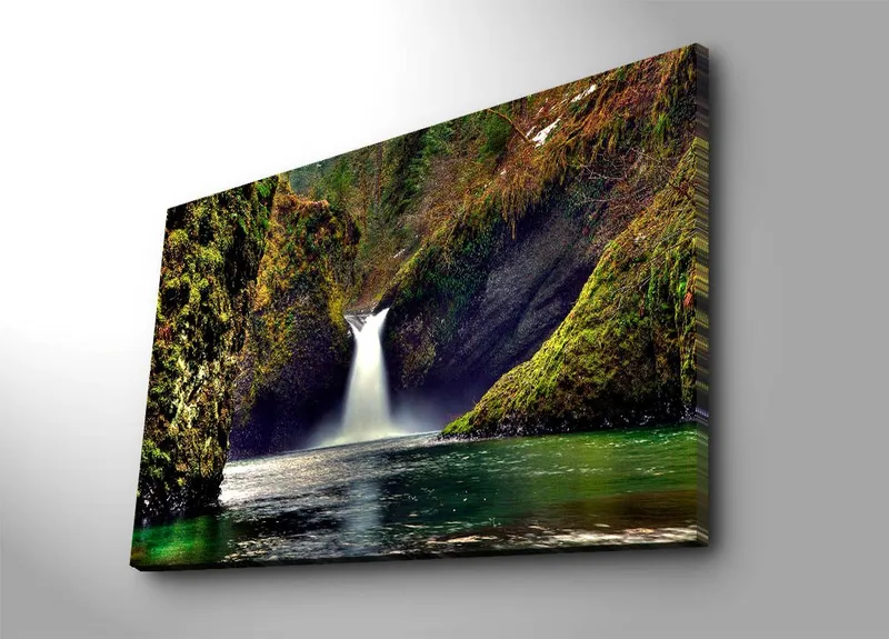 Lærredsbillede 70x100 cm - Smukt vandfald der flyder ned mellem grønne klipper i et naturskønt miljø, Grøn / Blå / Brun