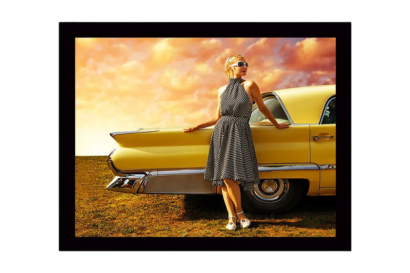 Indrammet trælærredstryk - 41x56 cm - Kvinde i prikket kjole læner sig op ad en veteranbil, Gul / Sort / Hvid